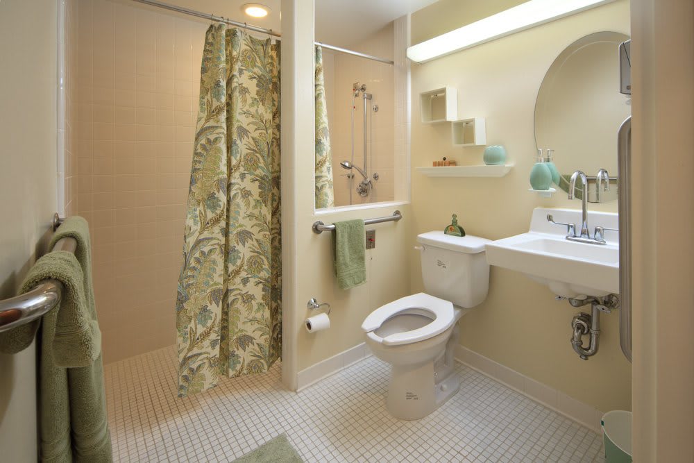 A modern bathroom featuring a shower with a floral curtain, toilet, and sink with green accents.