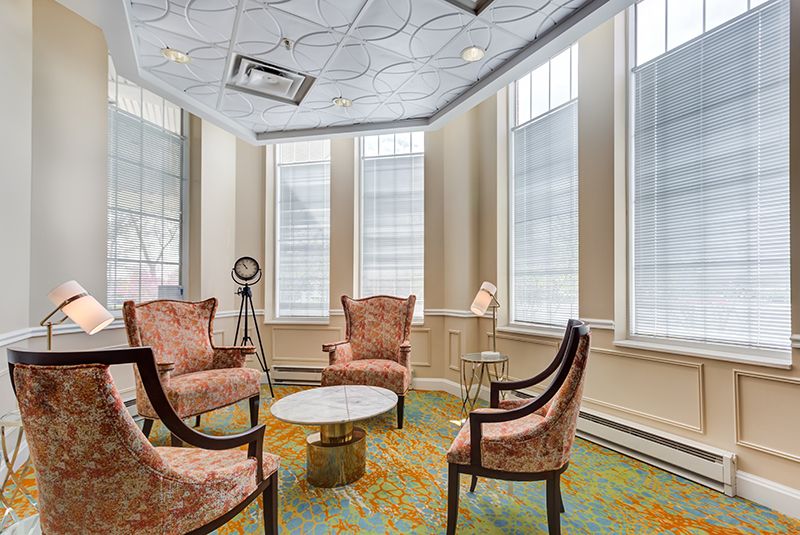A cozy sitting area with elegant chairs and a round table, illuminated by natural light from large windows.