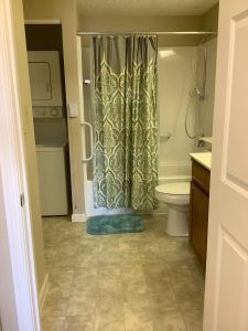 A view of a bathroom with an adjacent laundry area featuring a shower curtain, toilet, and washer-dryer unit.