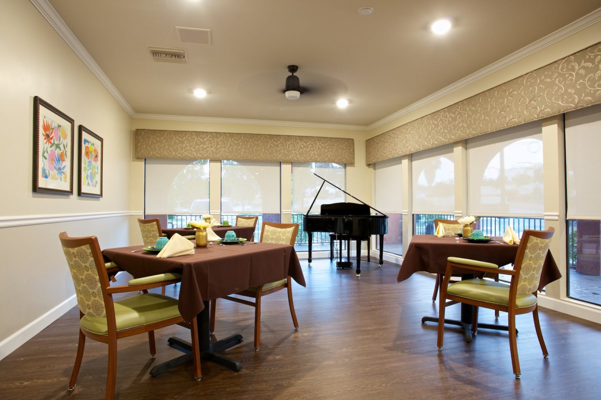 A cozy dining area with tables, chairs, and a grand piano in the corner.