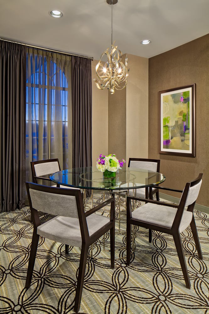 A stylish dining room with a glass table and elegant chairs, featuring a modern chandelier and artwork on the wall.
