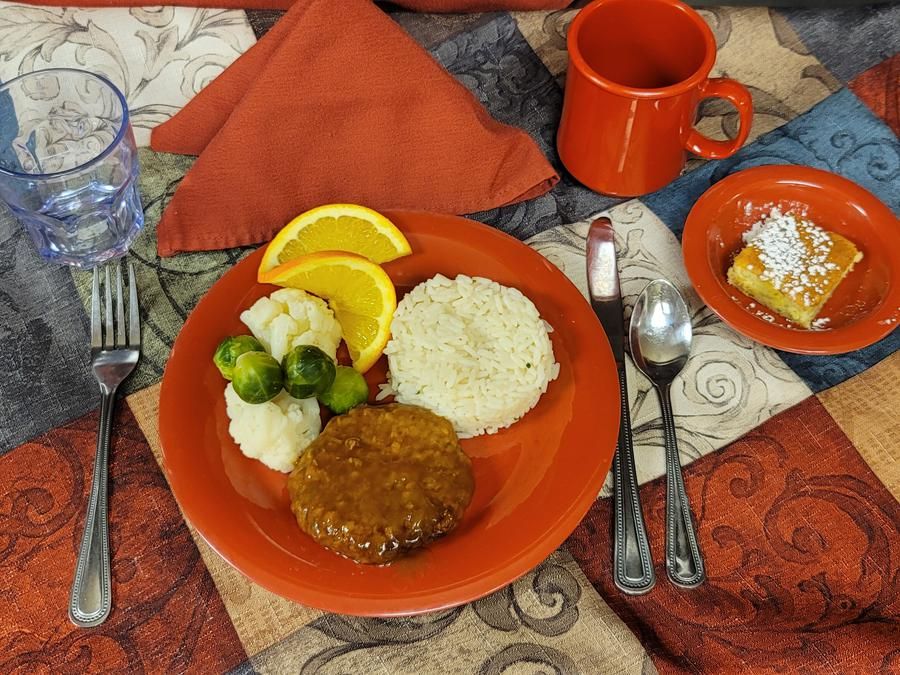 A meal setting with rice, brussels sprouts, a meat patty, and orange slices on a plate, accompanied by a dessert and a cup of coffee.