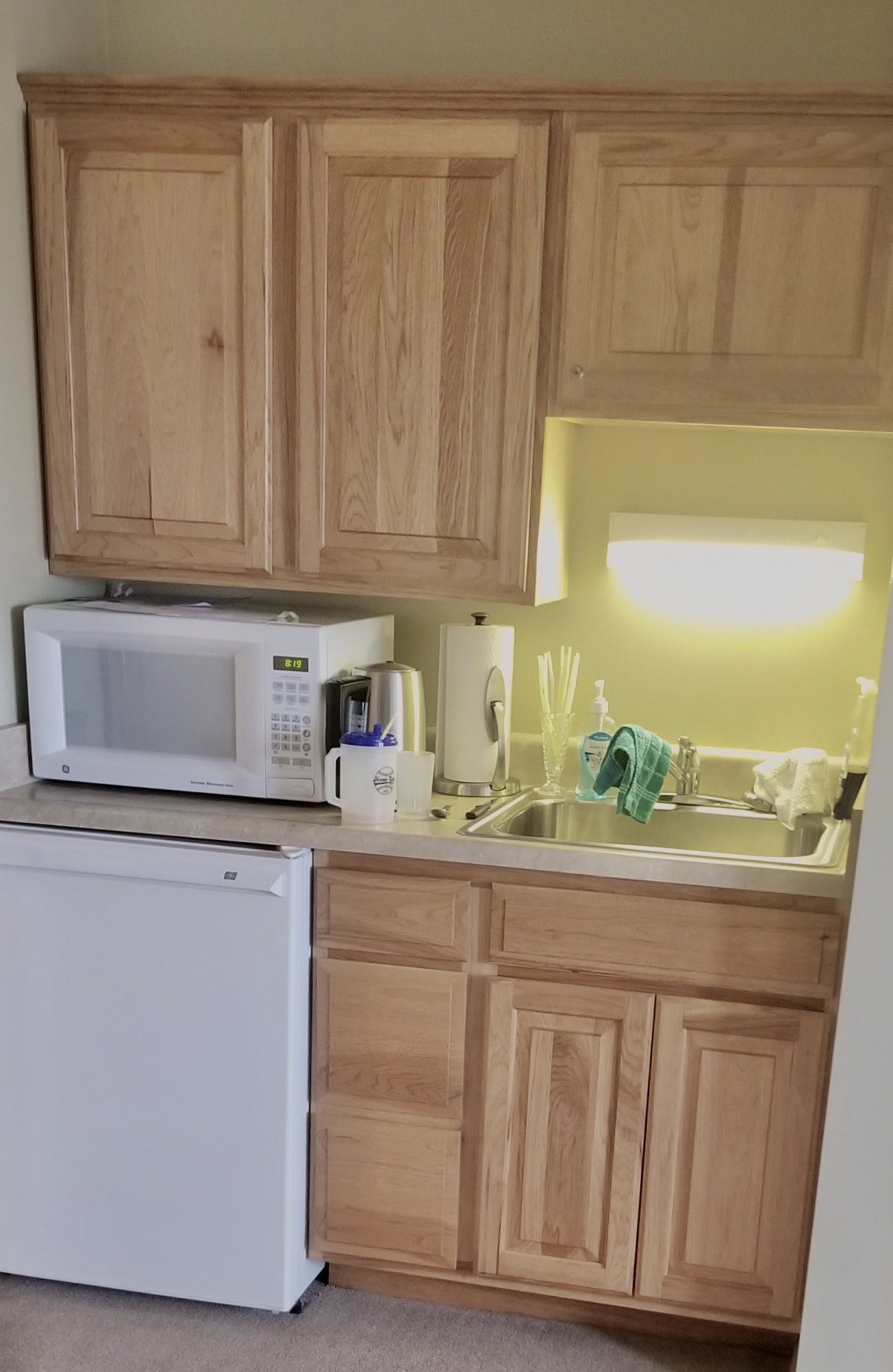A small kitchenette featuring a microwave, sink, and wooden cabinets.