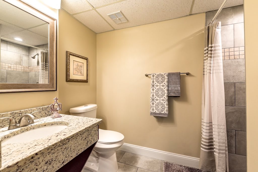 A clean and modern bathroom with beige walls, featuring a sink, mirror, toilet, and towel rack next to a shower curtain.