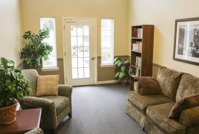 Cozy living room with a sofa, armchair, bookshelf, and natural light from windows.
