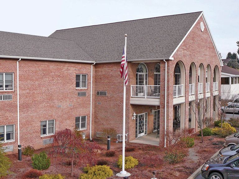 A two-story brick office building with a flagpole displaying the American flag in front of landscaped grounds.