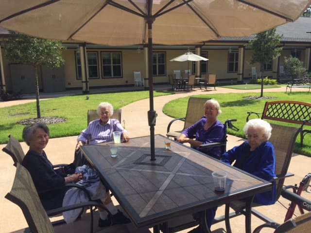 A group of seniors sitting together under a patio umbrella on a sunny day.