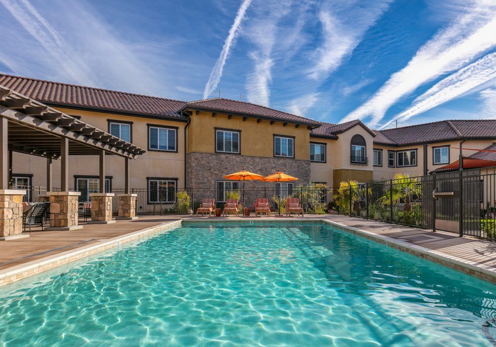 A luxurious residential building with a large outdoor swimming pool under a clear blue sky.
