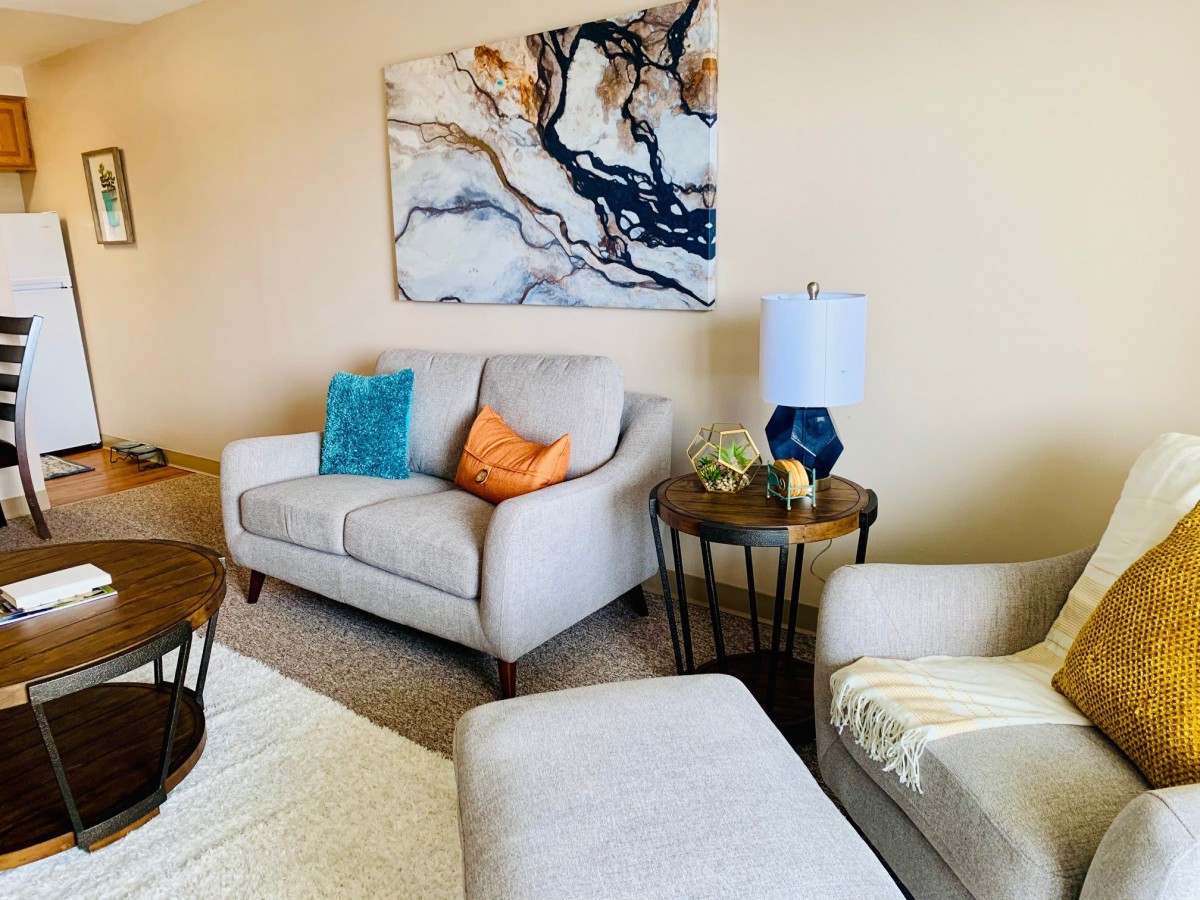 A cozy living room with a modern sofa and armchair, accented by colorful cushions and abstract artwork.