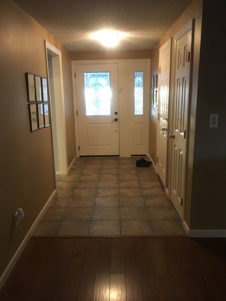 A well-lit hallway leading to a front door with tiled flooring.
