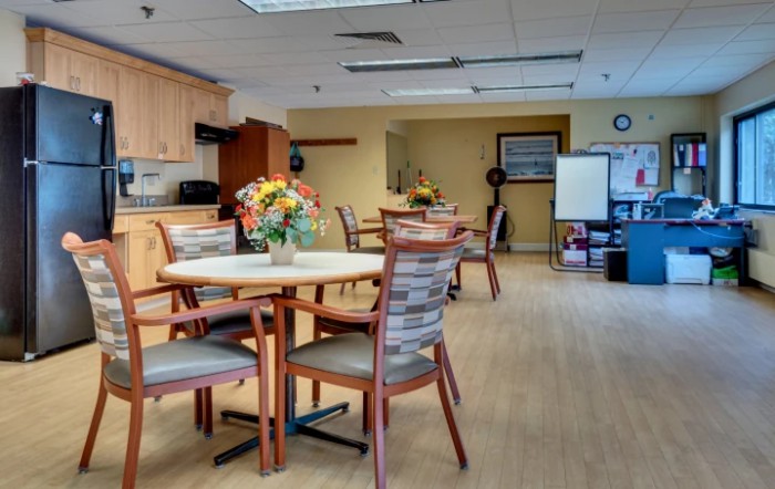 A spacious dining room with tables and chairs, featuring a kitchen area and decorative flowers.