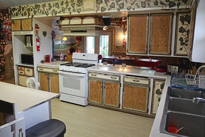 A vintage kitchen featuring wood cabinets, a white stove, and floral wallpaper.