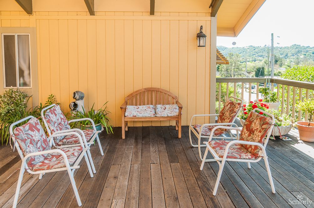 A cozy outdoor patio area with seating furniture, cushions, and decorative plants.