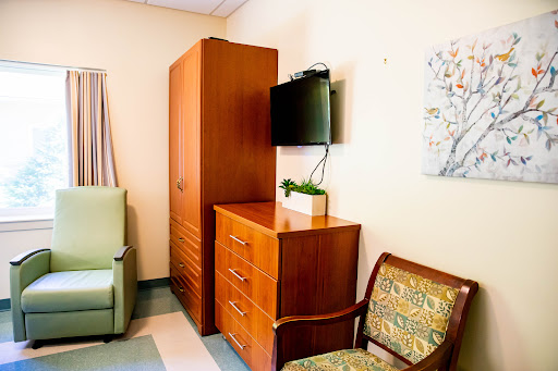 A well-furnished hospital room featuring a storage unit, a TV, and comfortable seating.