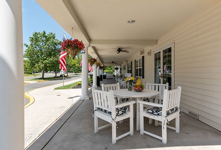 A cozy outdoor patio with white furniture, adorned with flowers and American flags, offering a serene spot for relaxation.