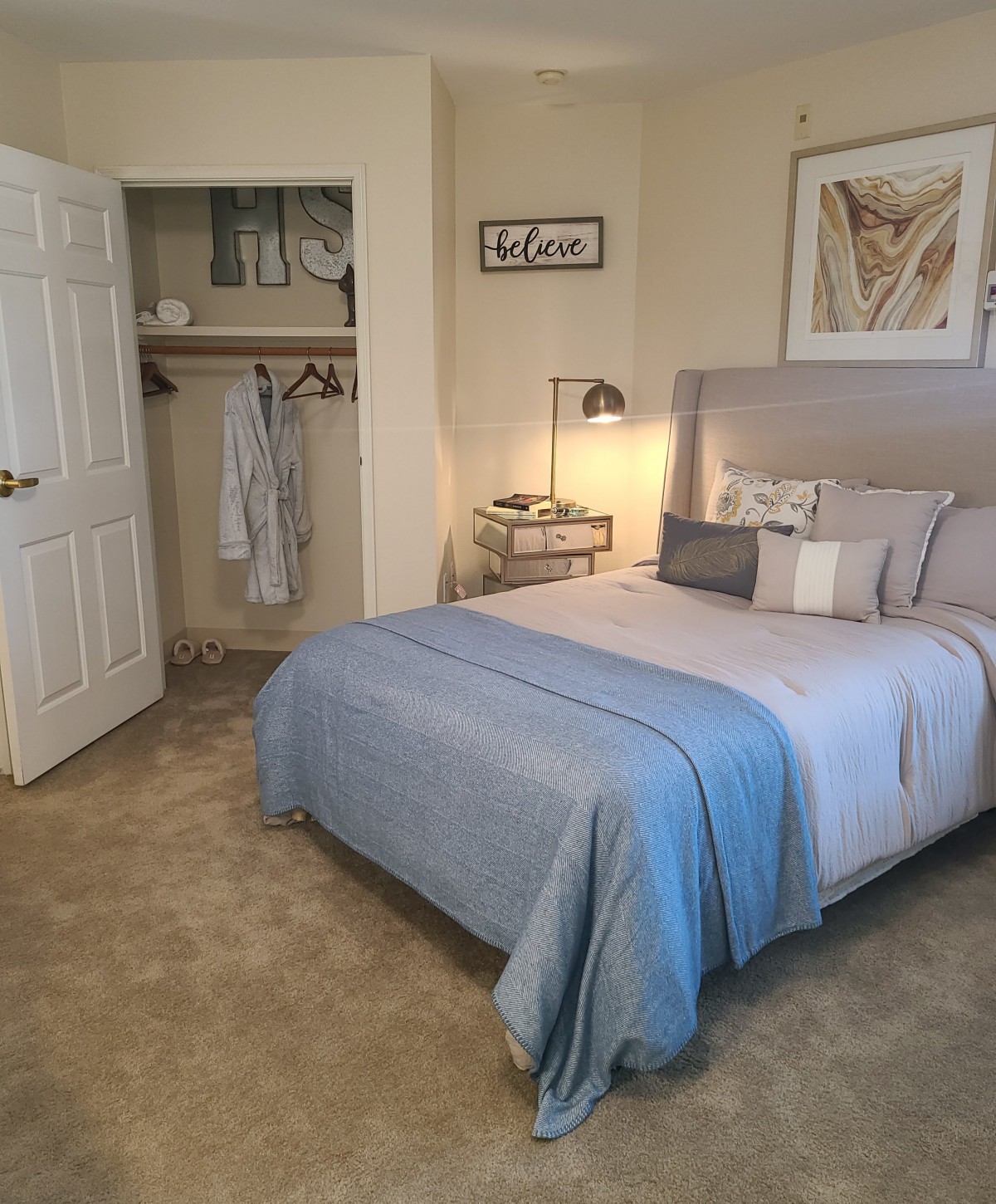 A cozy and neatly arranged bedroom with a bed, side table, lamp, and open closet.