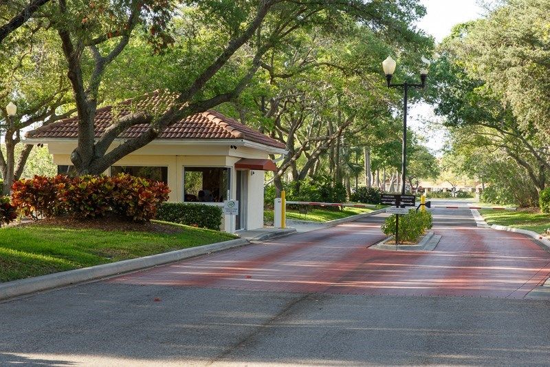 A gated community entrance with a guardhouse surrounded by lush greenery and well-maintained landscaping.