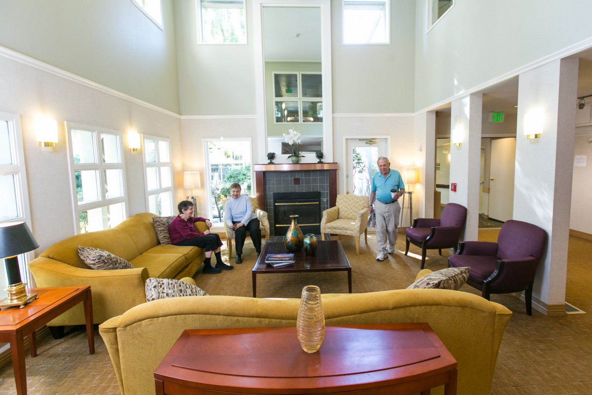 A spacious living room with high ceilings, featuring several people gathered around the fireplace and comfortable seating.