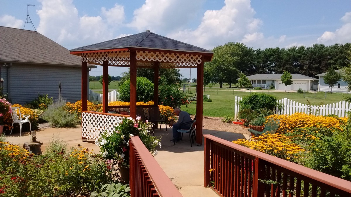 A beautiful garden with a wooden gazebo surrounded by vibrant flowers under a sunny sky.