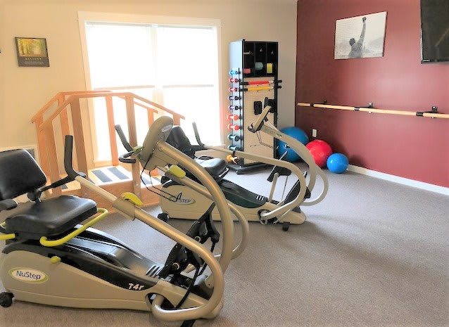A well-lit gym with cardio machines and exercise equipment.