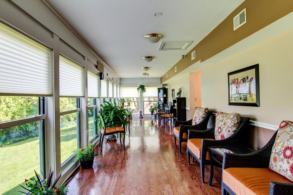 A bright hallway with large windows, greenery, and comfortable seating.