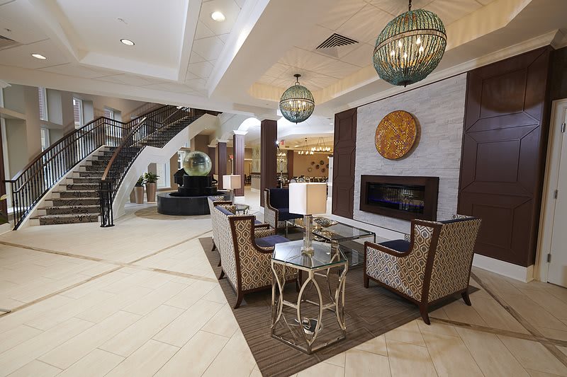 A modern hotel lobby with elegant seating, decorative lighting, and a grand staircase.