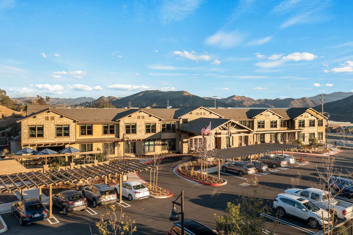 A scenic view of a building complex with a parking lot in the foreground and mountains in the background under a clear sky.