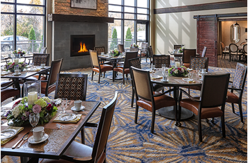 A cozy restaurant dining area with tables and chairs arranged near a fireplace.