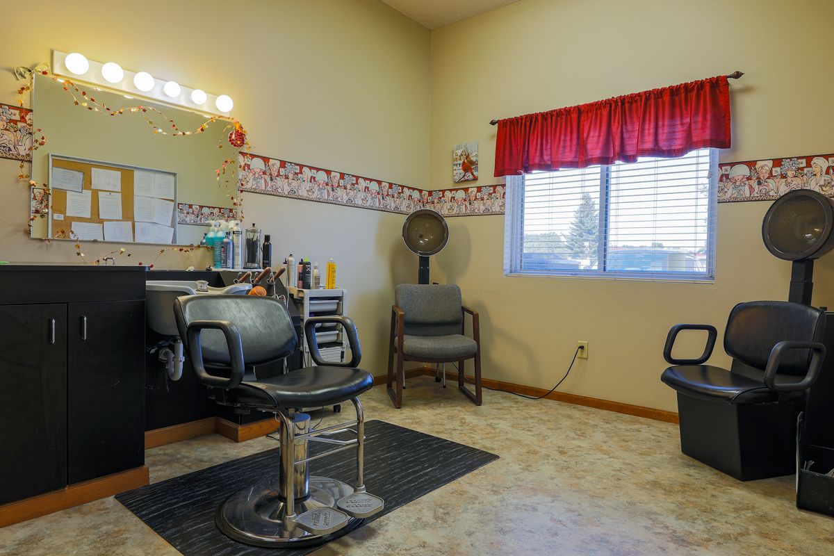 A cozy hair salon interior with styling chairs, a mirror, and a window with red curtains.