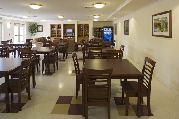 An empty dining area with tables and chairs, featuring a vending machine in the background.