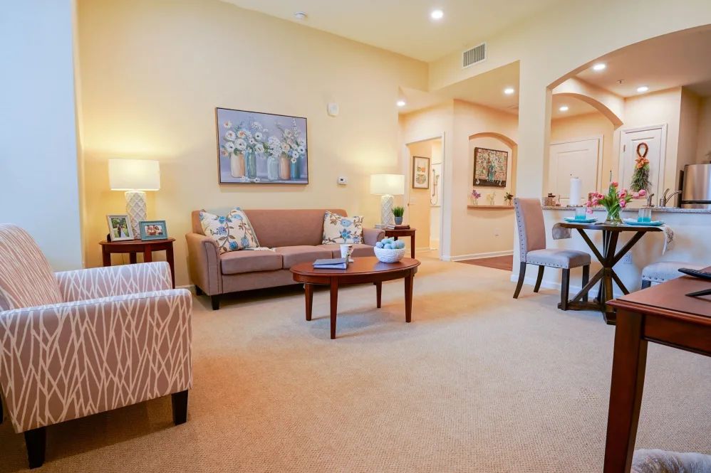 A cozy living room with a sofa, armchair, and coffee table, featuring tasteful artwork and soft lighting.