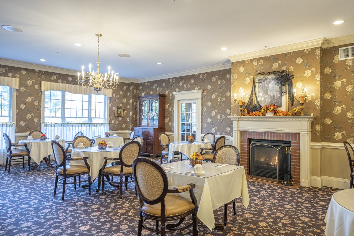 An elegant dining room with a chandelier, decorated with floral wallpaper and a fireplace.