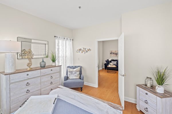 A cozy bedroom with a dresser, accent chair, and natural light streaming through the window.