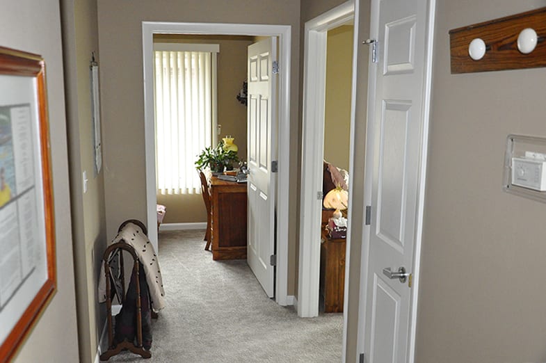 A hallway with multiple open doors leading to a room with a desk and window blinds.