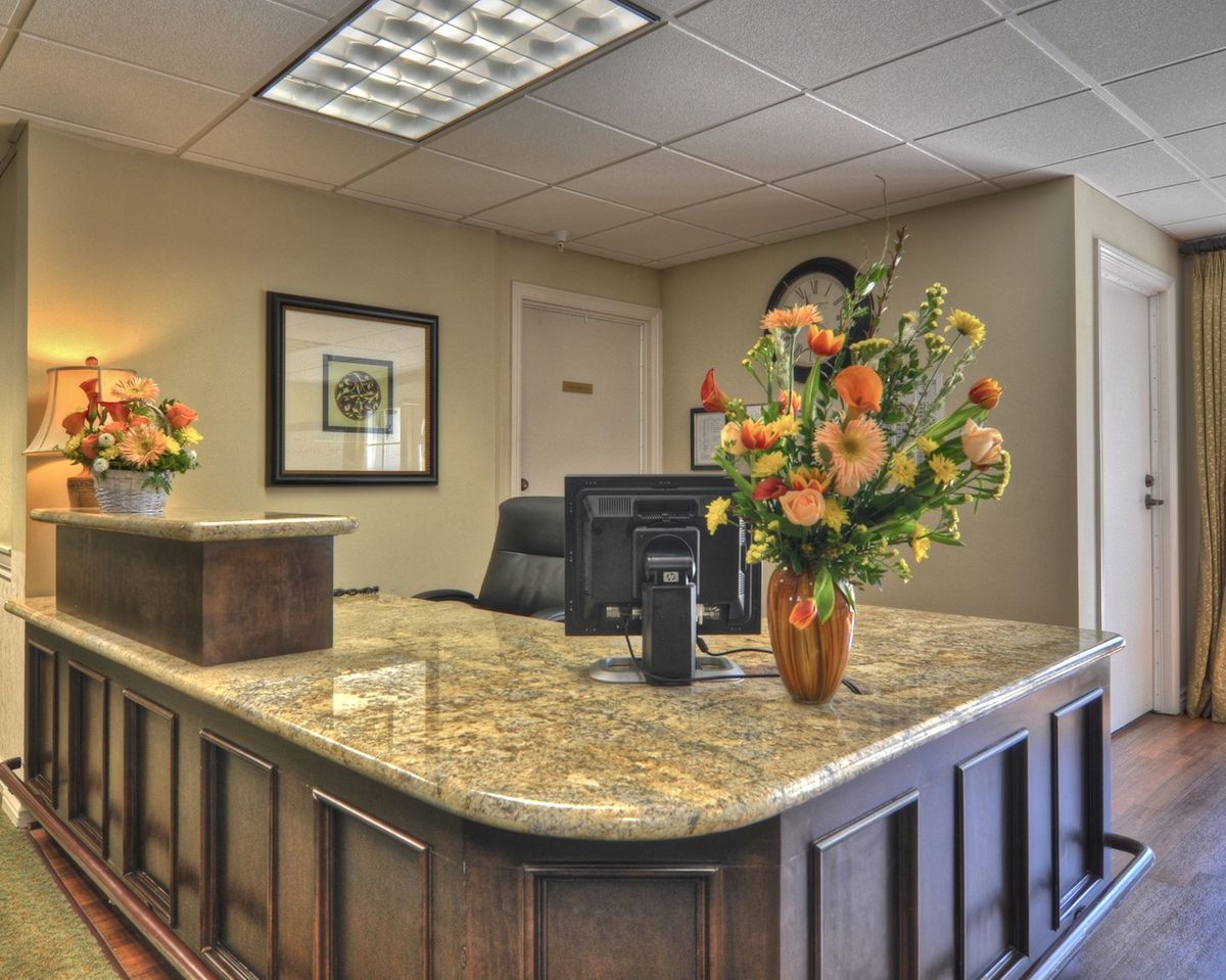 A well-organized office reception area with a granite desk and floral decorations.