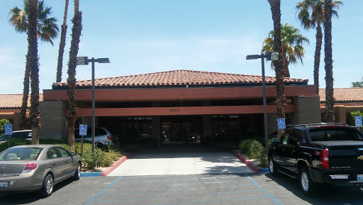 A sunny day at a modern building with a tiled roof and palm trees lining the parking area.