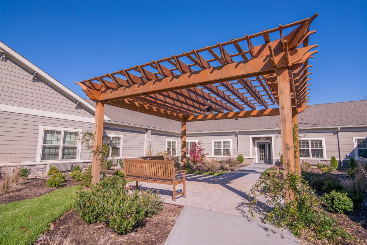 A wooden pergola with a bench in a landscaped garden outside a residential building.