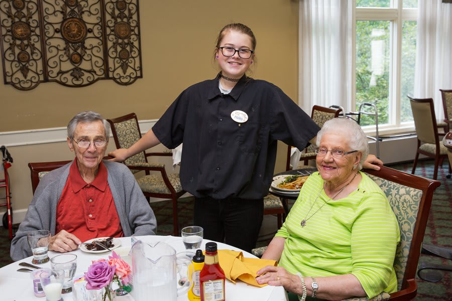 A server stands behind two senior patrons at a dining table, creating a pleasant restaurant setting.