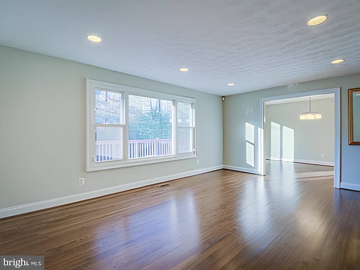 A spacious, empty room with hardwood flooring and a large window letting in natural light.