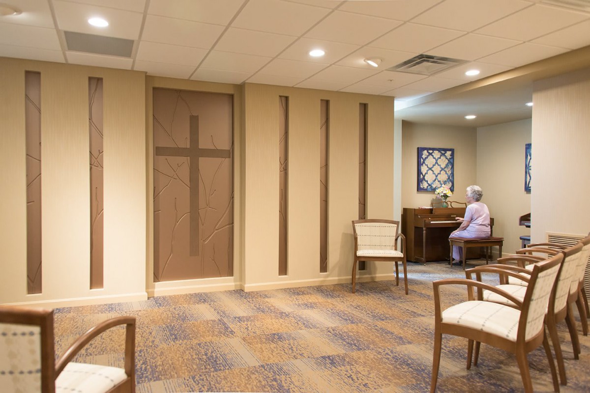 A quiet chapel interior with a cross, chairs, and a piano.