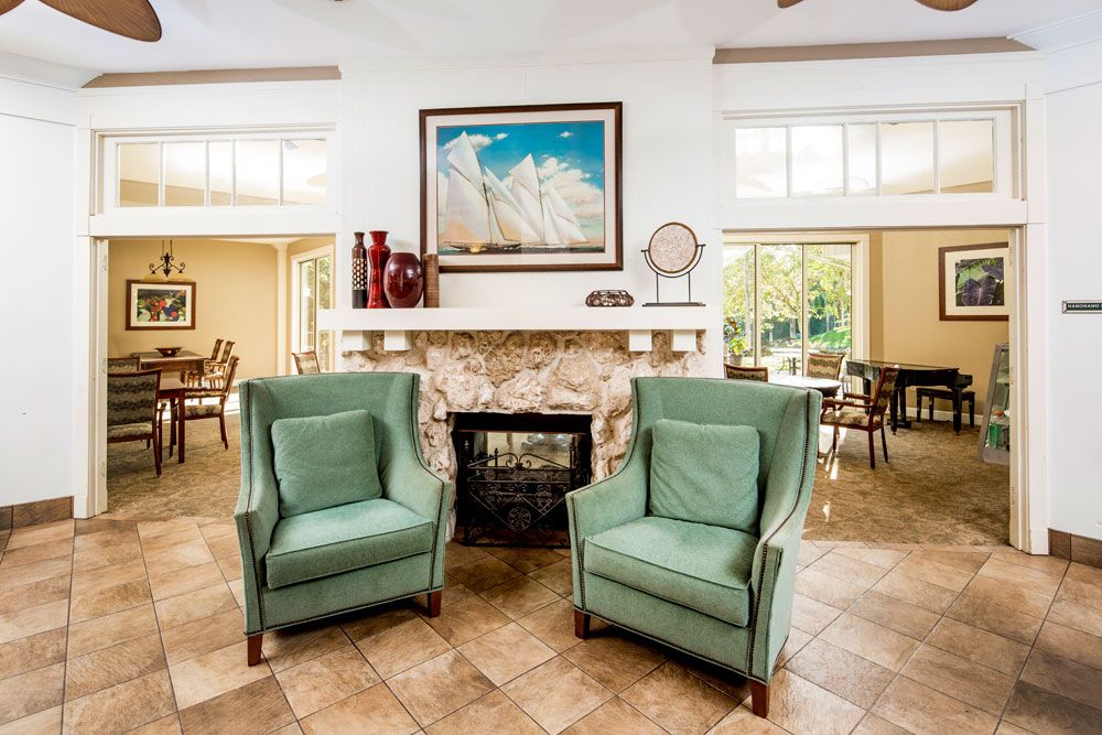 A cozy living room with two green armchairs in front of a stone fireplace, adorned with artwork and decor.