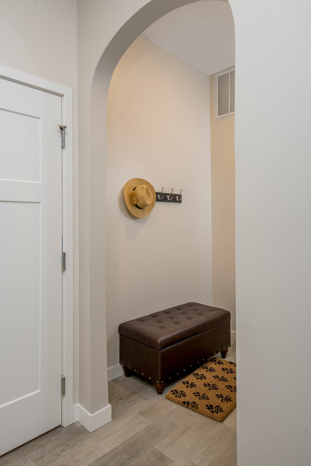 A small entryway with a bench, hat on the wall hook, and a patterned rug.
