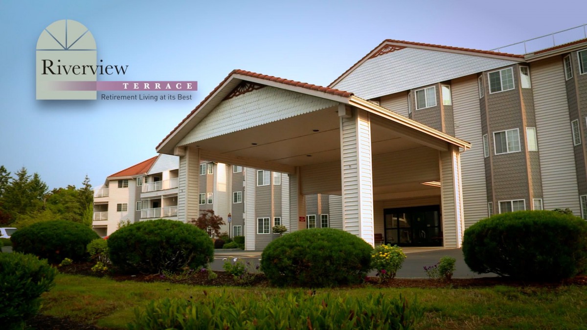 The image shows the exterior of a hotel entrance with landscaped greenery.