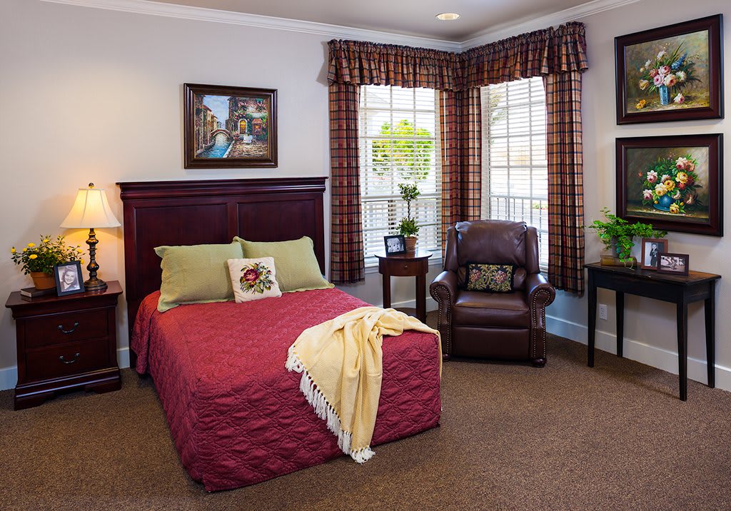 Cozy bedroom with a neatly arranged bed, armchair, and large windows.