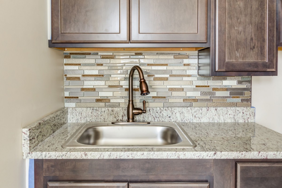 A modern kitchen sink area with a stylish backsplash and granite countertop.