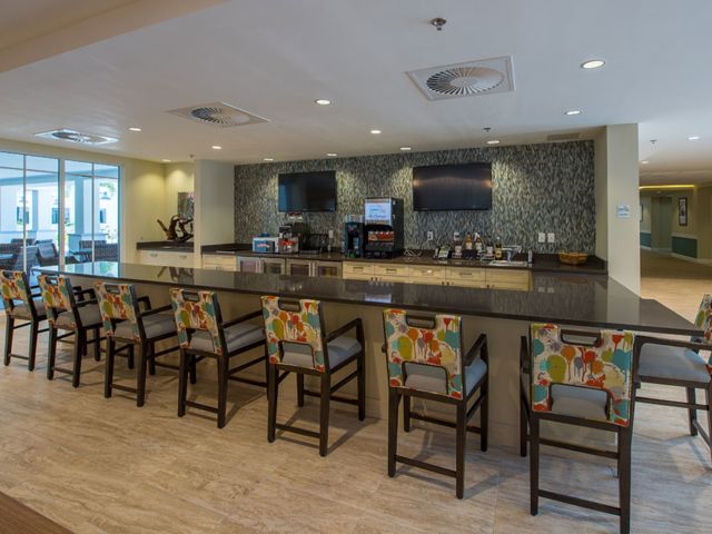 A modern bar area with a sleek counter, colorful chairs, and televisions mounted on the wall.
