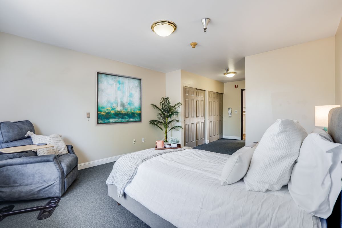 A modern bedroom with minimalist decor, featuring a bed, artwork on the wall, and a potted plant.