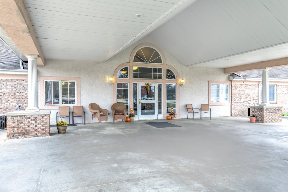 A building entrance with a covered porch, featuring several chairs and decor.