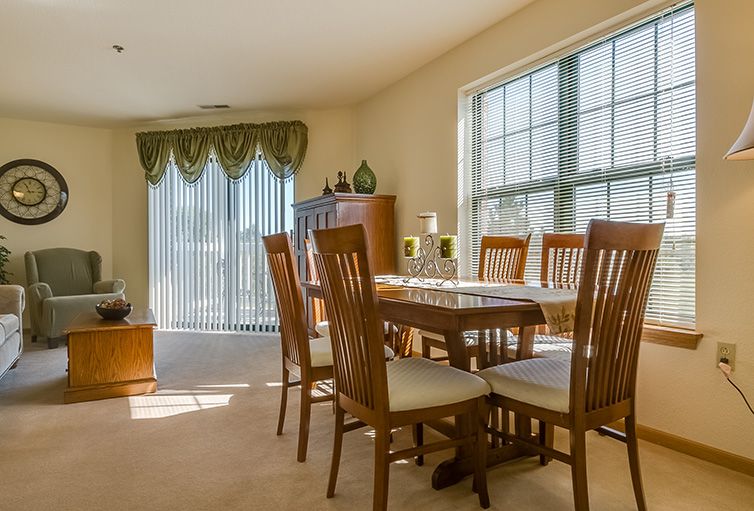 A sunlit dining room with a wooden table and chairs beside large windows.