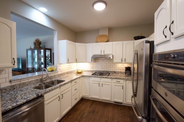 A modern kitchen featuring white cabinets and granite countertops, complemented by stainless steel appliances and a hardwood floor.